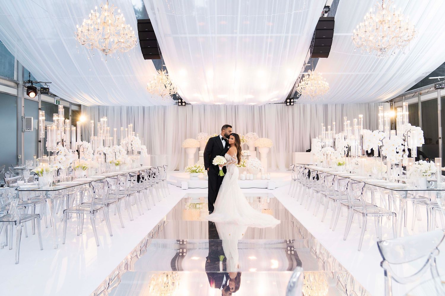 Modern all-white wedding venue interior with crystal chandeliers and elegant seating.