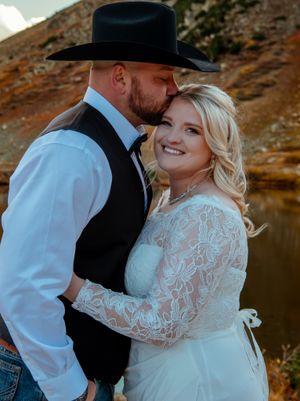 A couple shares an intimate moment during their western-themed wedding photoshoot against a scenic mountain backdrop.