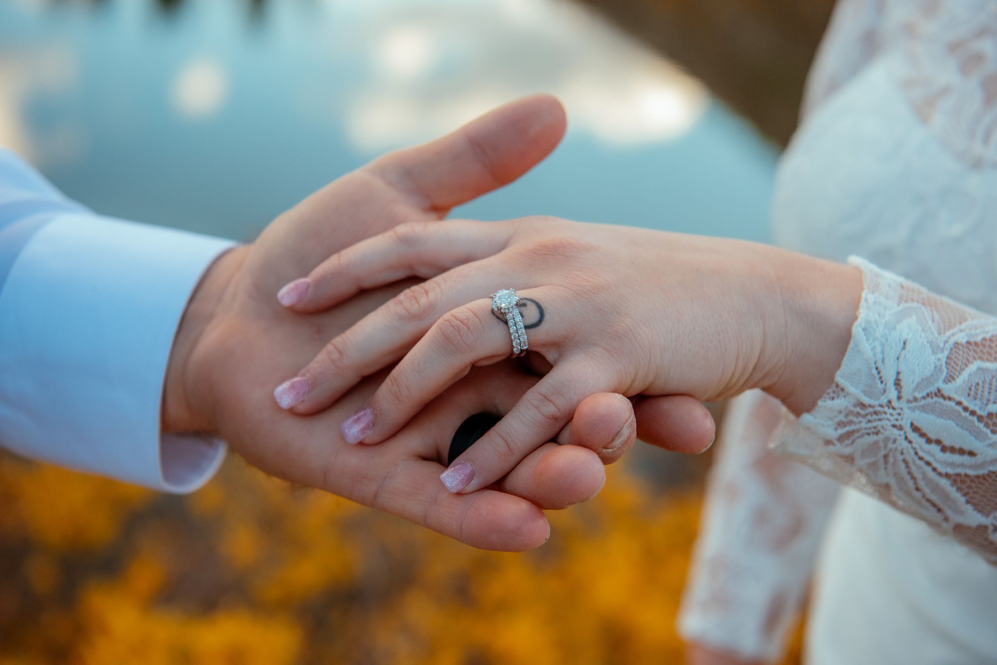 Close-up view of hands wearing wedding rings with soft golden sunlight in the background.