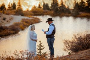 Romantic sunset engagement photo session by a lake with pine trees silhouetted against golden sky.