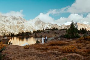 Mountain landscape panorama with evergreen trees and dramatic cloudy sky reflected in alpine lake at sunset.