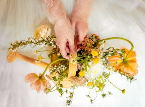 Bride's hands arranging delicate yellow and green floral bouquet details.