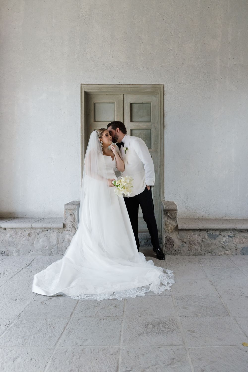 A romantic wedding couple shares an intimate moment against a minimalist white wall and doorway.