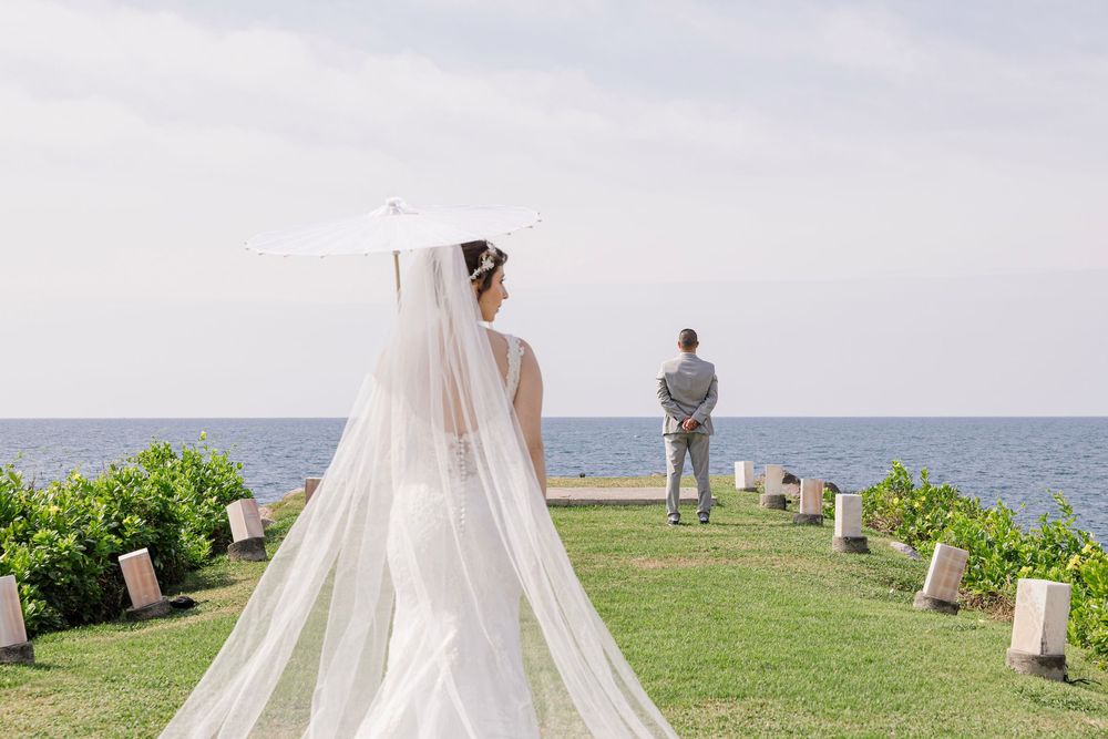 Un velo de novia blanco vaporoso ondea con la brisa del mar sobre un pintoresco fondo costero con exuberante vegetación.
