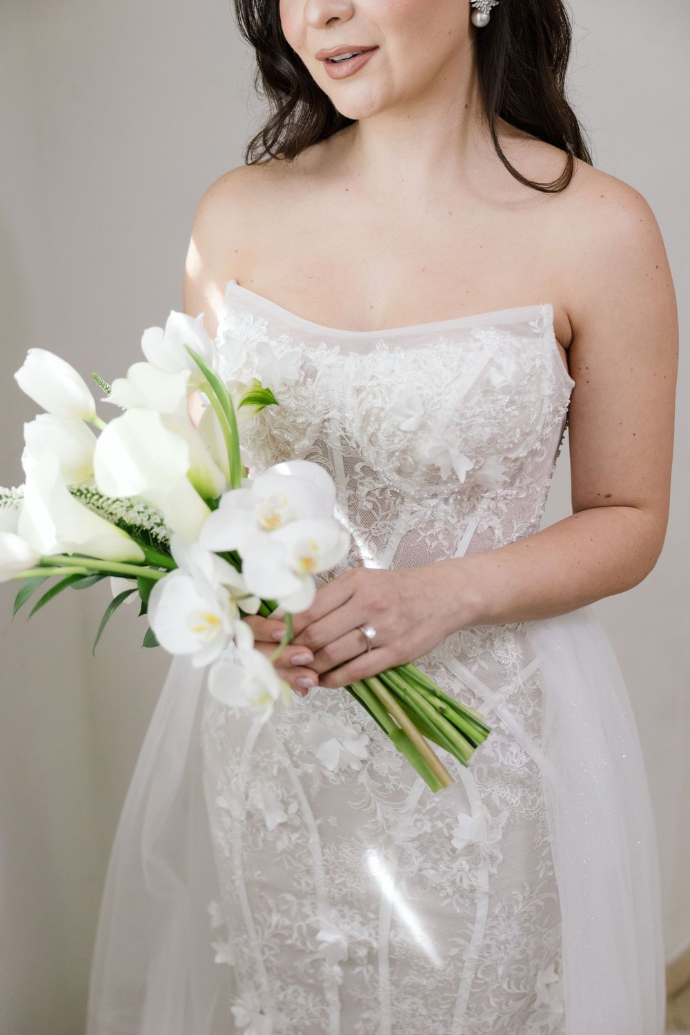 Bride in white lace wedding dress holding a bouquet of white lilies.