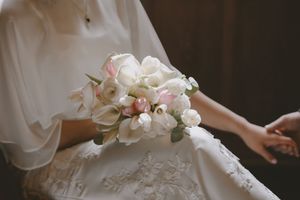 Bride in white lace gown holding elegant bouquet of pink roses and white calla lilies on her wedding day.