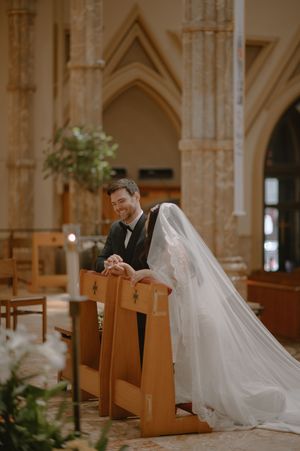 Bride and groom kneeling at church pew during wedding ceremony in stunning Gothic cathedral.