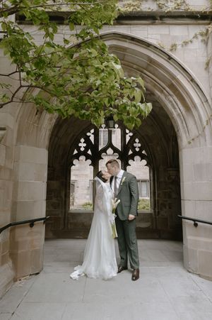 Bride and groom share a romantic moment under a Gothic stone archway, surrounded by lush greenery at their wedding venue.