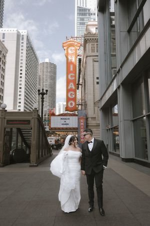 Bride and groom pose before iconic Chicago Theatre marquee on their wedding day.