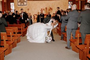 Bride and groom share a romantic dip kiss in church aisle during wedding ceremony with guests applauding.
