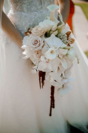 Bride in white lace gown holding elegant cascading wedding bouquet with roses, calla lilies, and orchids.