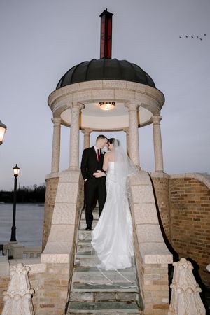 Bride and groom share romantic moment under stone gazebo at dusk on wedding day.