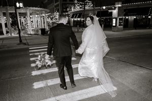 Bride and groom crossing a city street at night, holding hands, in black and white wedding photo.