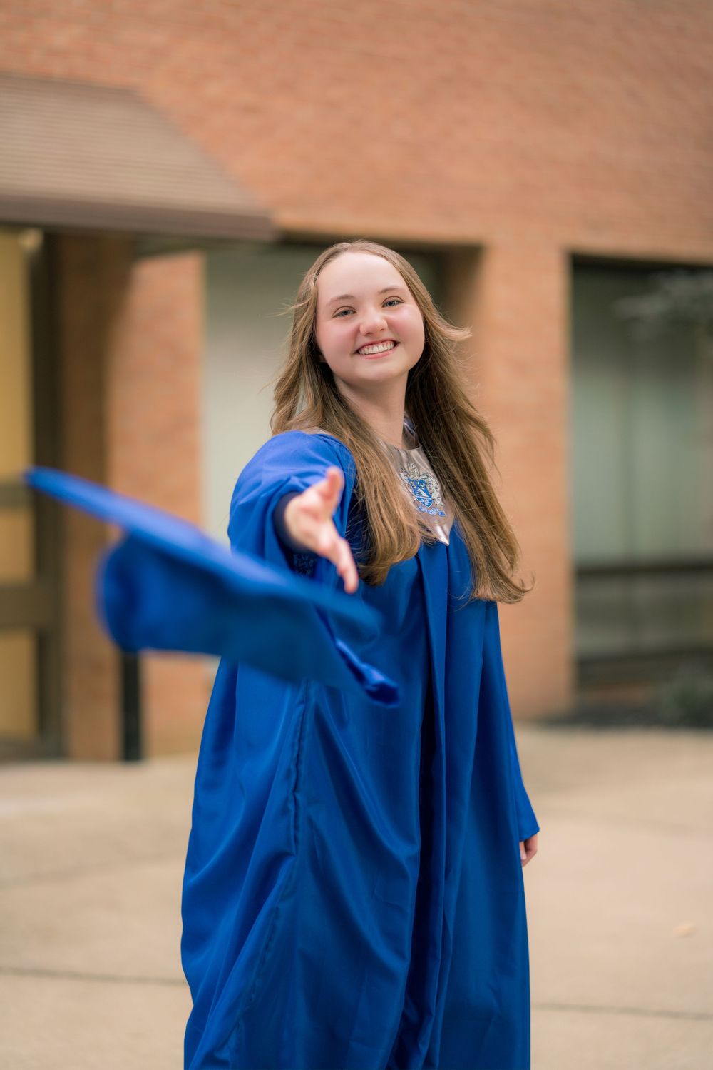 Graduate in blue cap and gown twirling and celebrating outdoors.