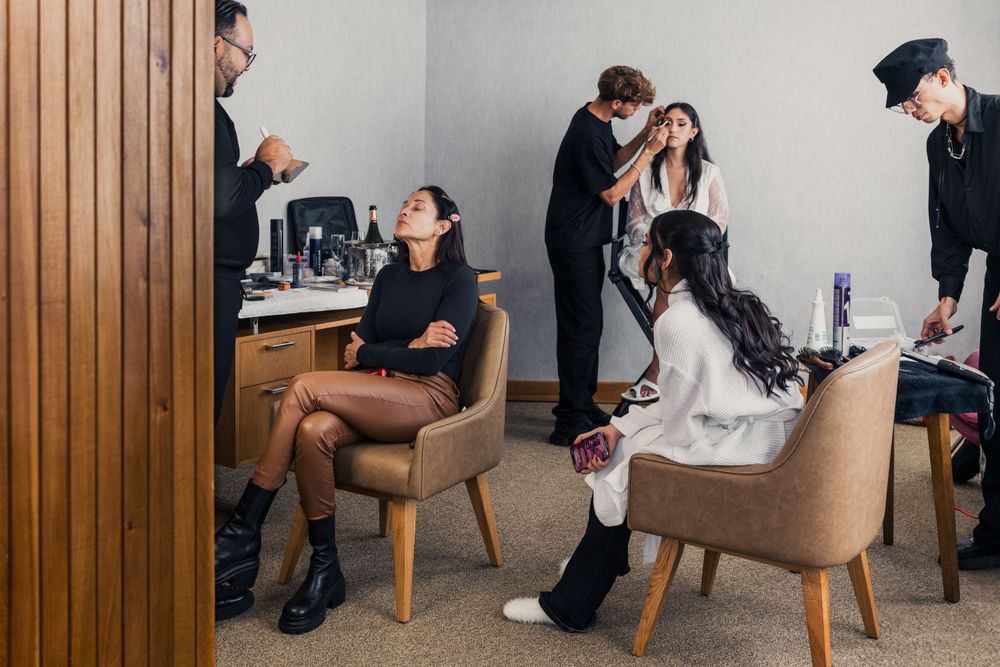 Wedding preparation scene with people getting styled and made up in elegant chairs.