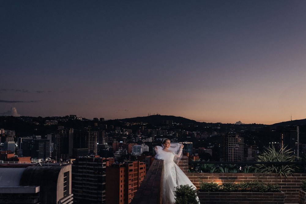 A wedding dress silhouette against a cityscape at dusk with twinkling lights below.