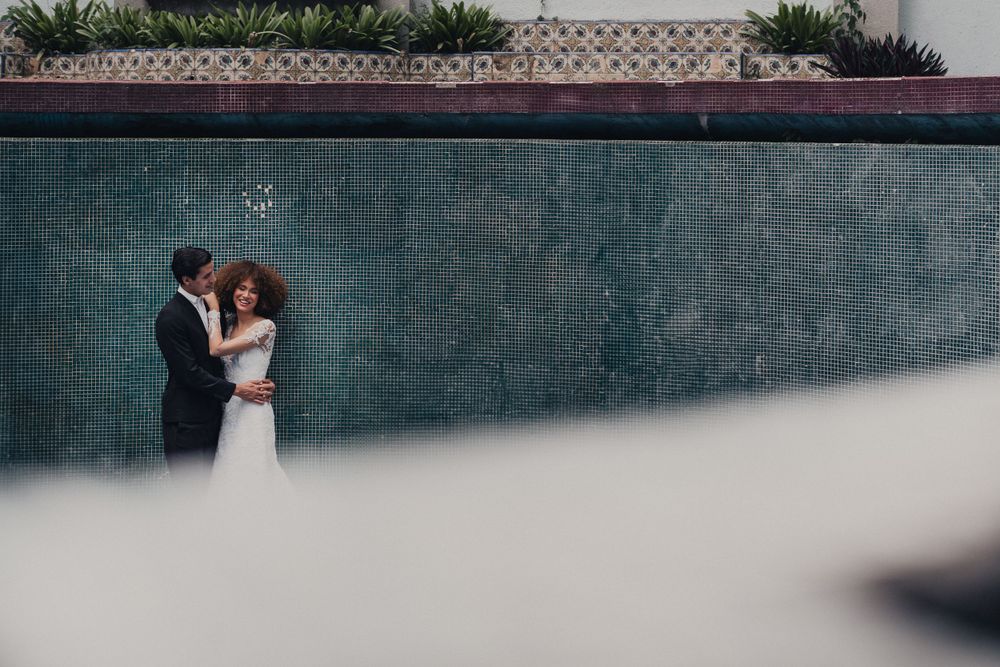 Intimate wedding moment captured against a teal wall with soft focus foreground creating romantic framing.