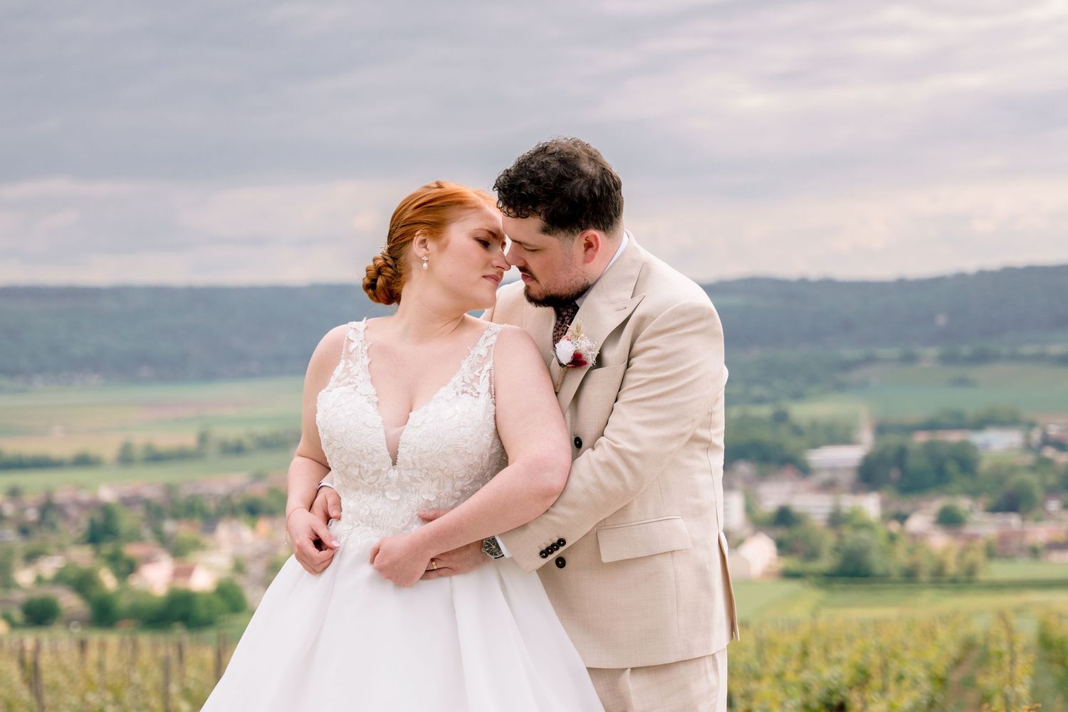 A couple in formal white attire walks and laughs together on a gravel path at dusk.