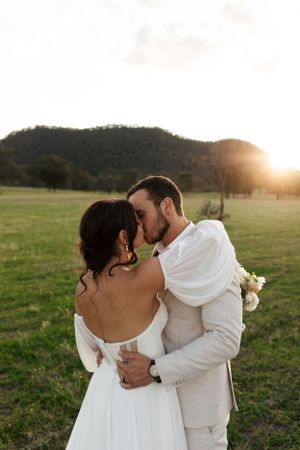 Intimate wedding moment captured during golden hour in an open field with mountains.