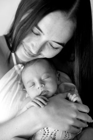 Black and white photo of a smiling mother tenderly holding her sleeping newborn baby close to her chest.