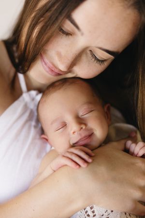 A tender moment as a young mother gazes lovingly at her sleeping newborn baby cradled in her arms.