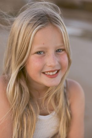 Smiling young blonde girl with freckles and long hair posing outdoors at the beach.