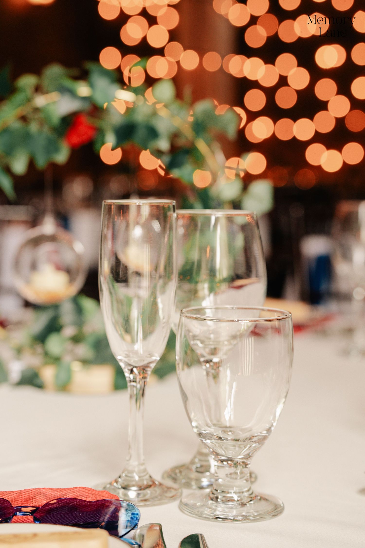 Wedding reception table setting with empty wine glasses and bokeh lights.