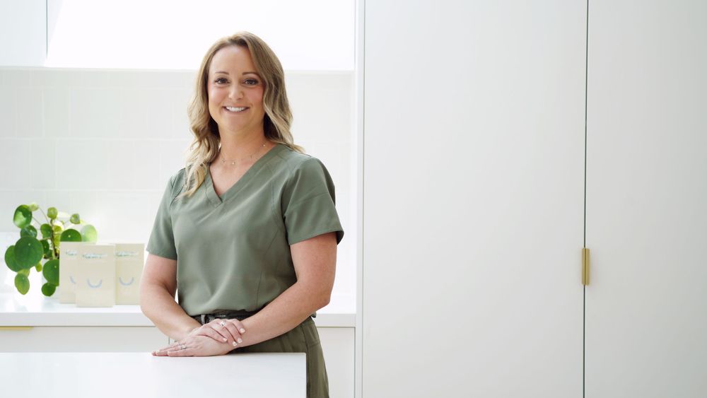 Person in sage green top standing by bright window in minimal interior.