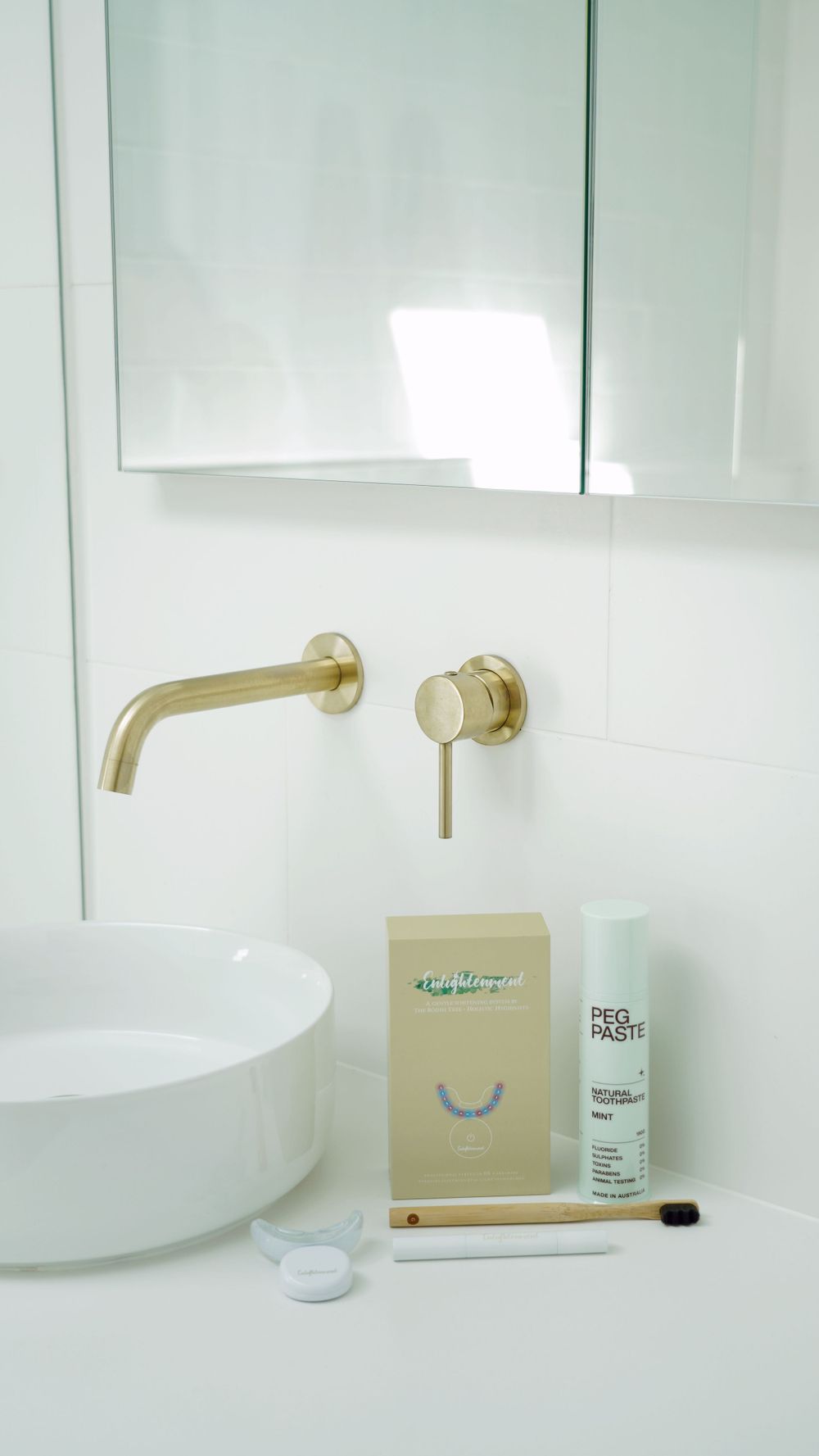 Modern white bathroom with gold fixtures and minimal toiletries on counter.