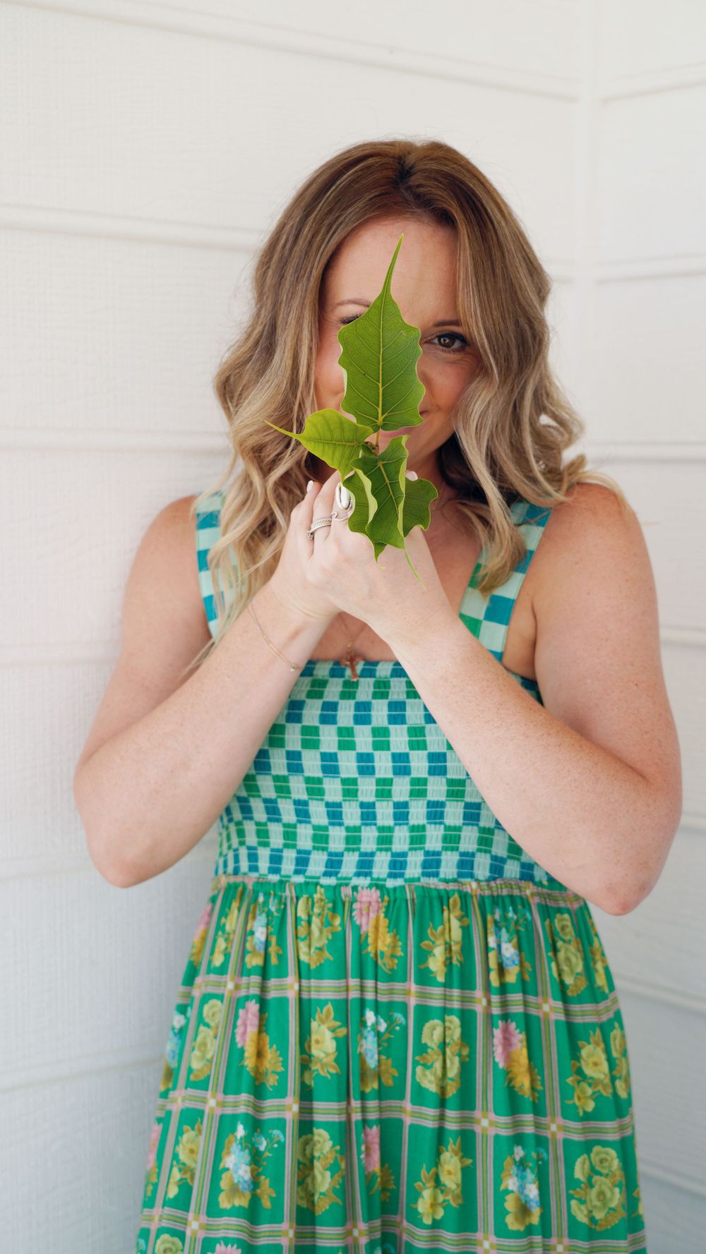 Person in green checkered dress playfully holding leaf over face.