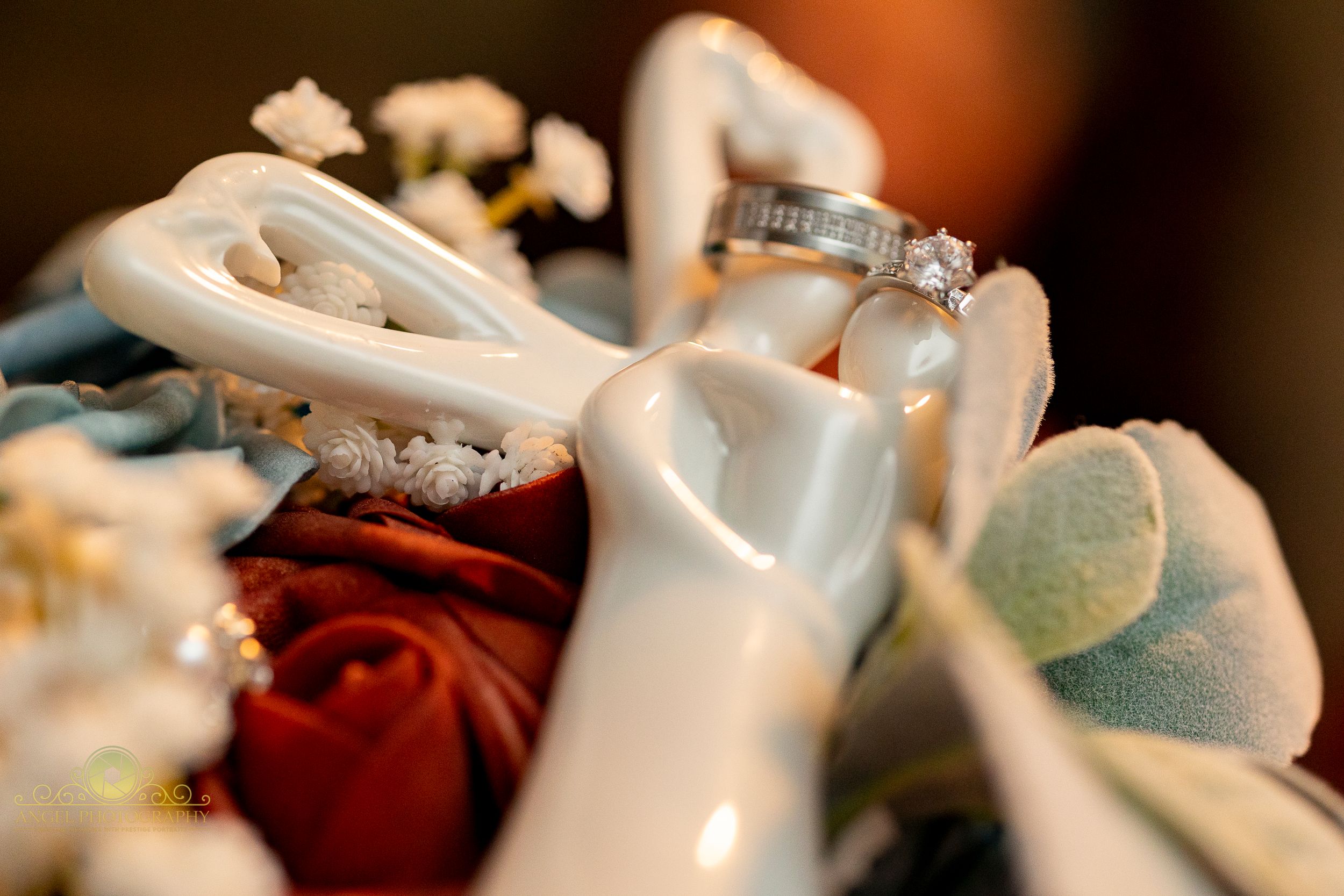 White wedding shoes next to red and blue floral decorations with a sparkling engagement ring on display.