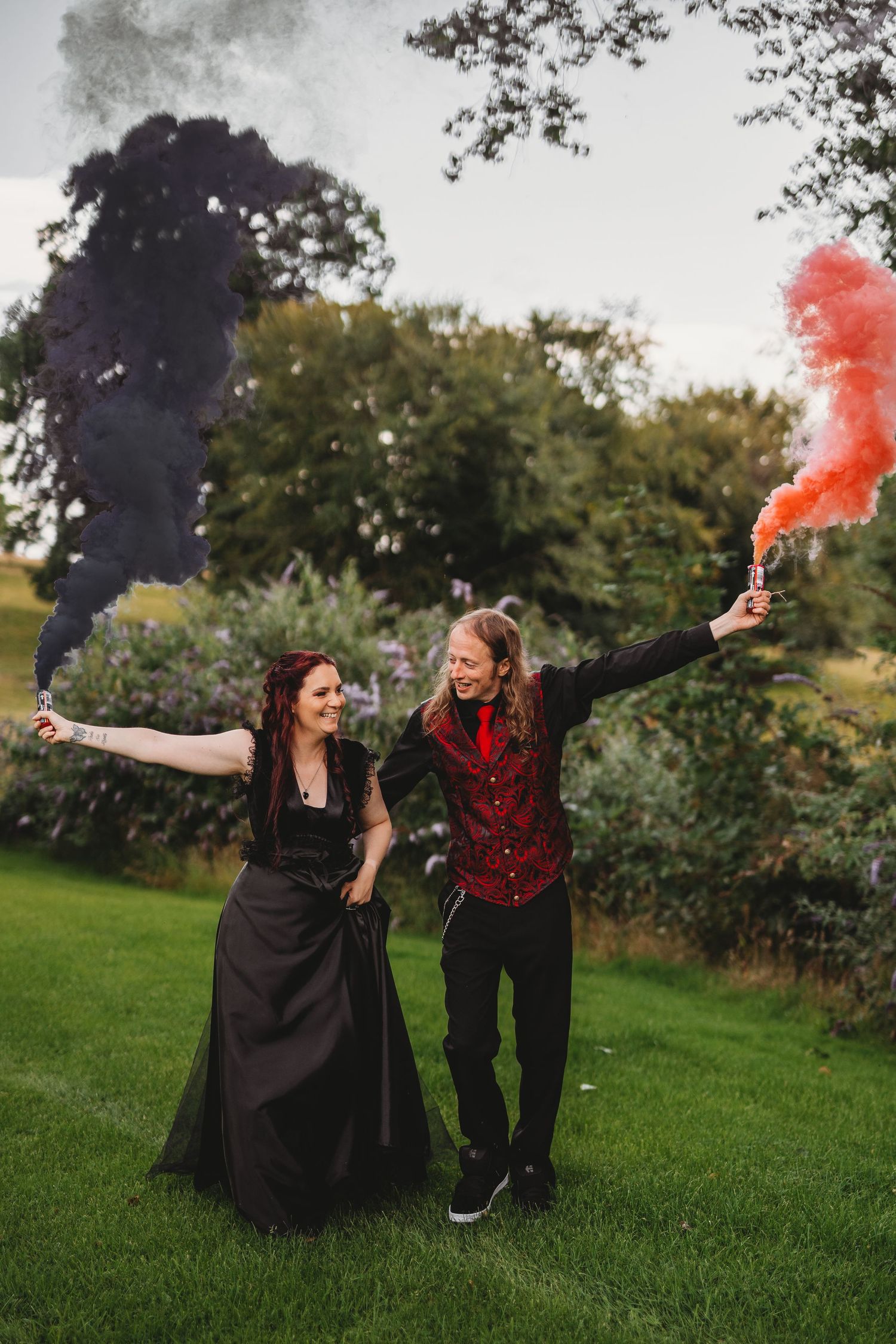 Couple with red and black smoke bombs posing dramatically on grass.