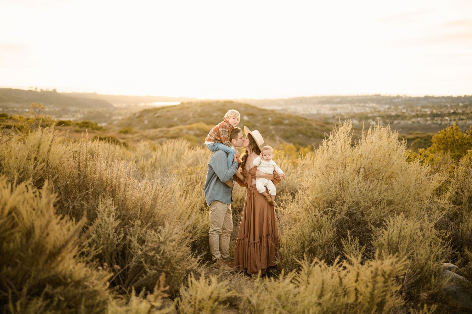 A family of four enjoying a moment together in an open field at sunset.