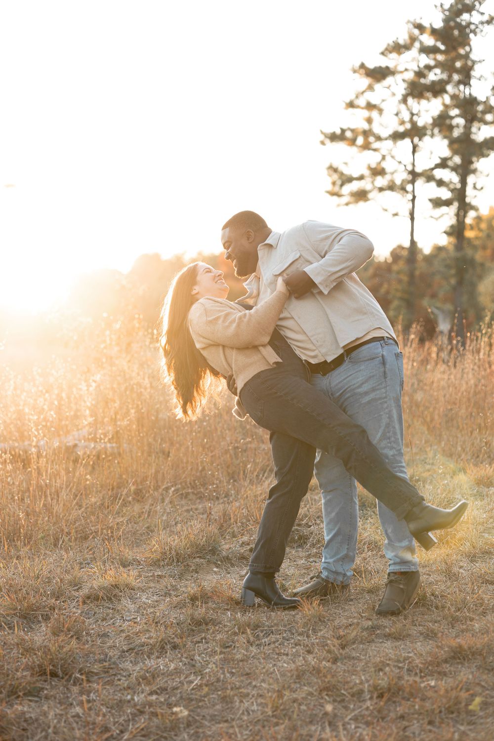 A couple dances and embraces in a golden sunlit field during sunset.