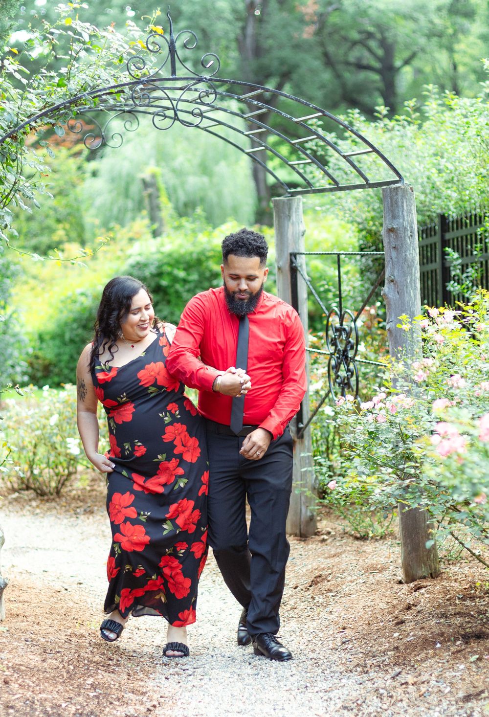 Playful wedding photos along a garden path with stone walls and metal arbor.