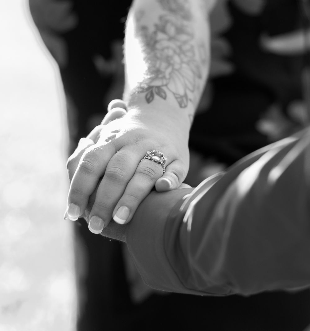 Black and white close-up of hands with wedding rings and tattoo details.