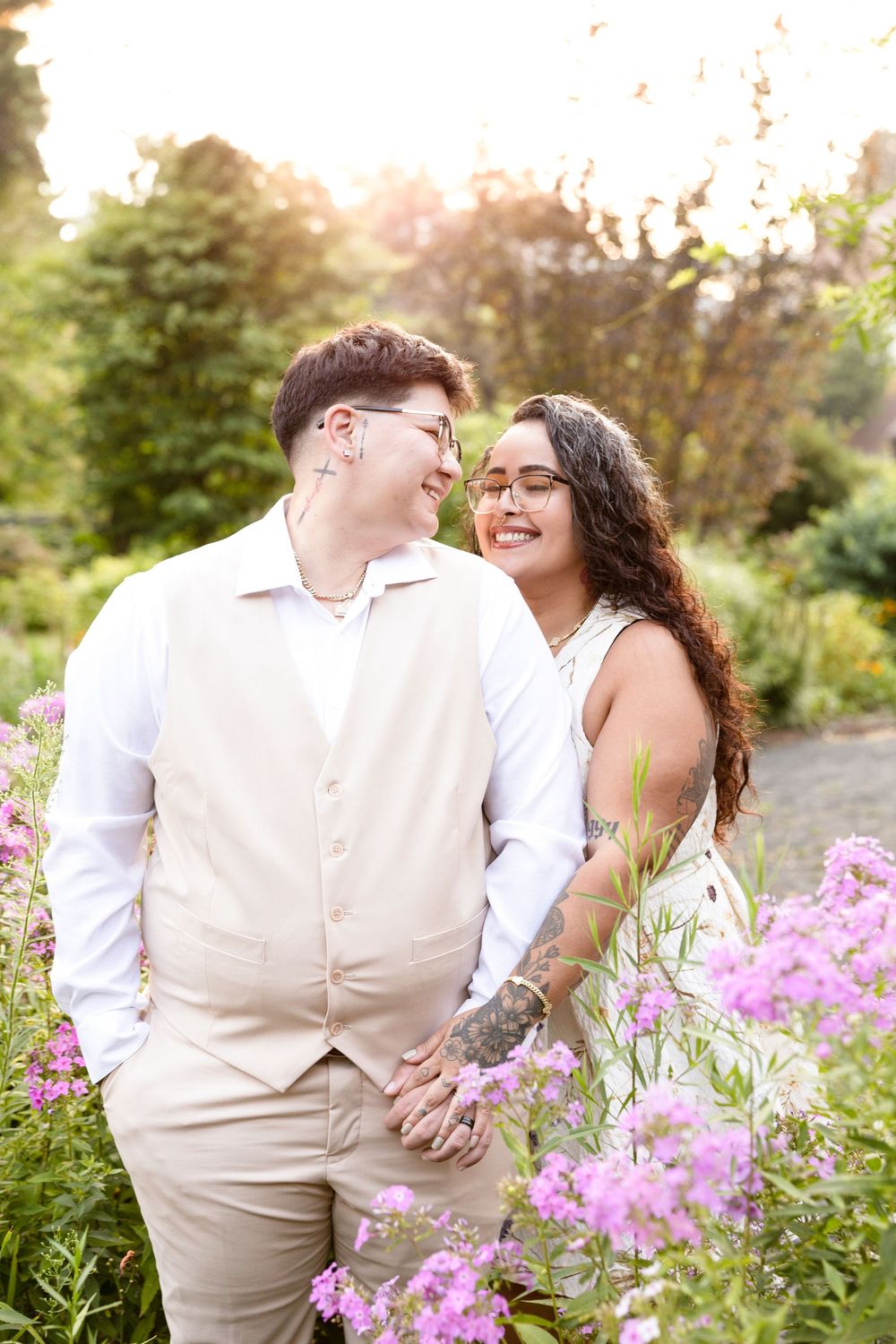 Couple sharing intimate moments among pink flowers in garden setting at sunset.