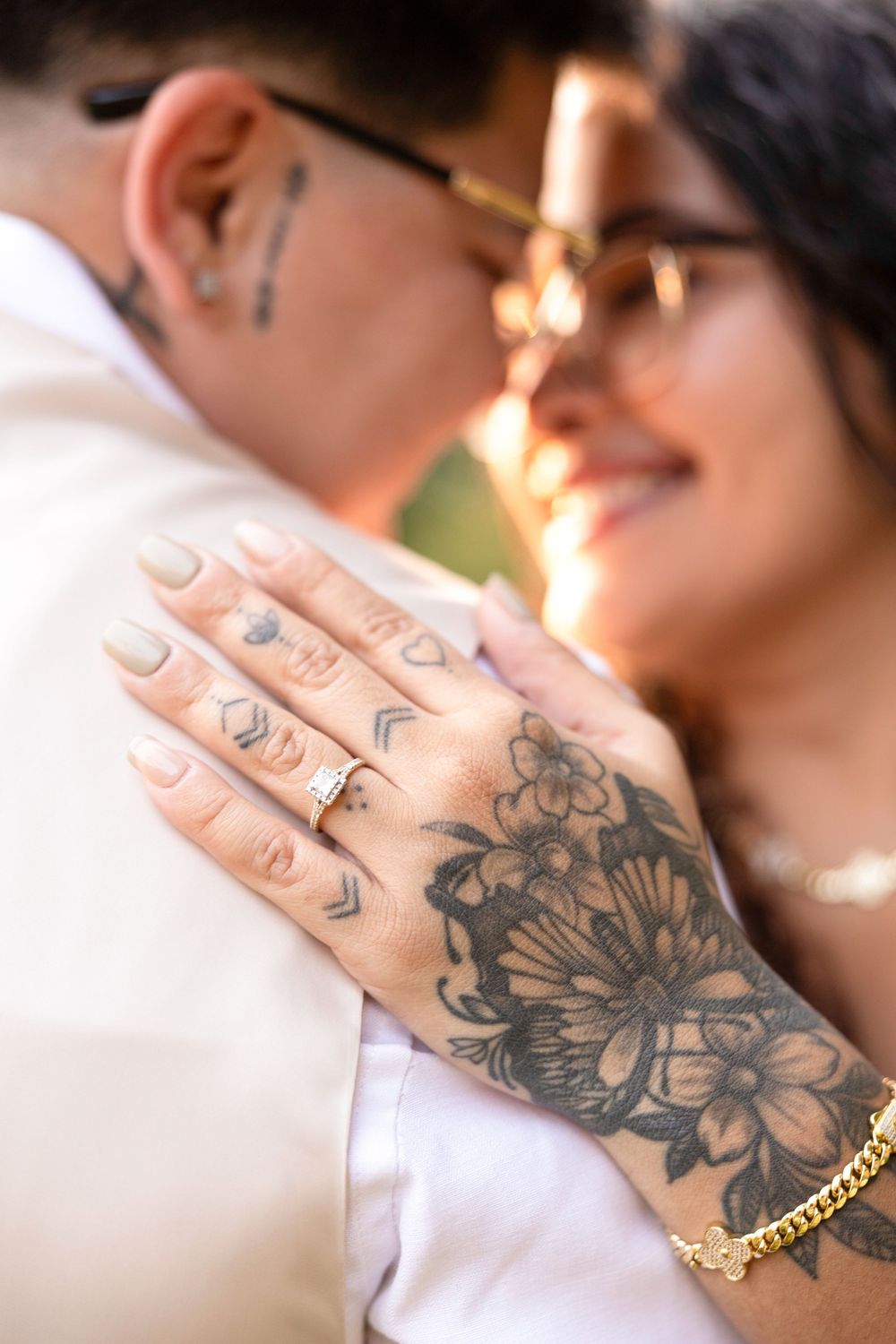 Close-up of a floral tattoo and engagement ring on hand against white clothing.