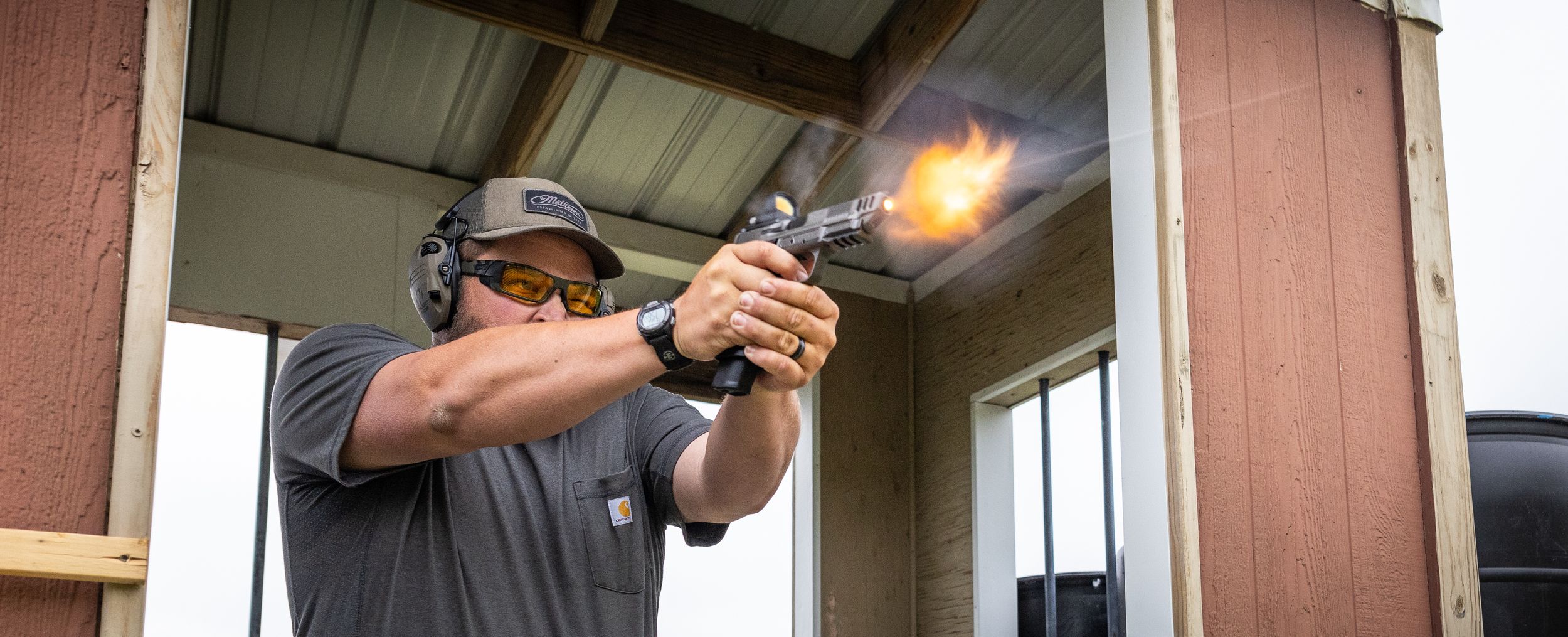 Person demonstrating proper firearm handling technique at an indoor shooting range.