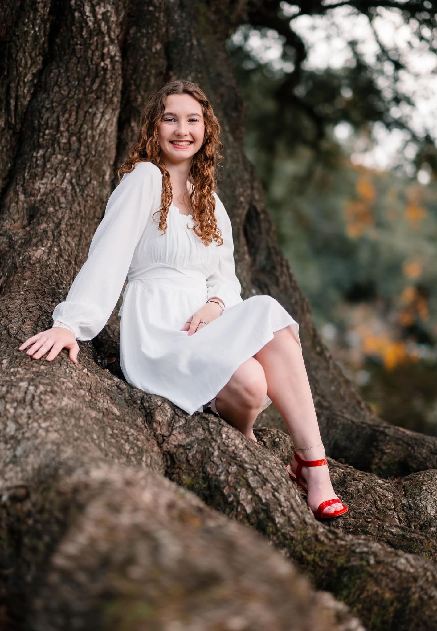 Senior sitting on oak tree in white dress and red heels