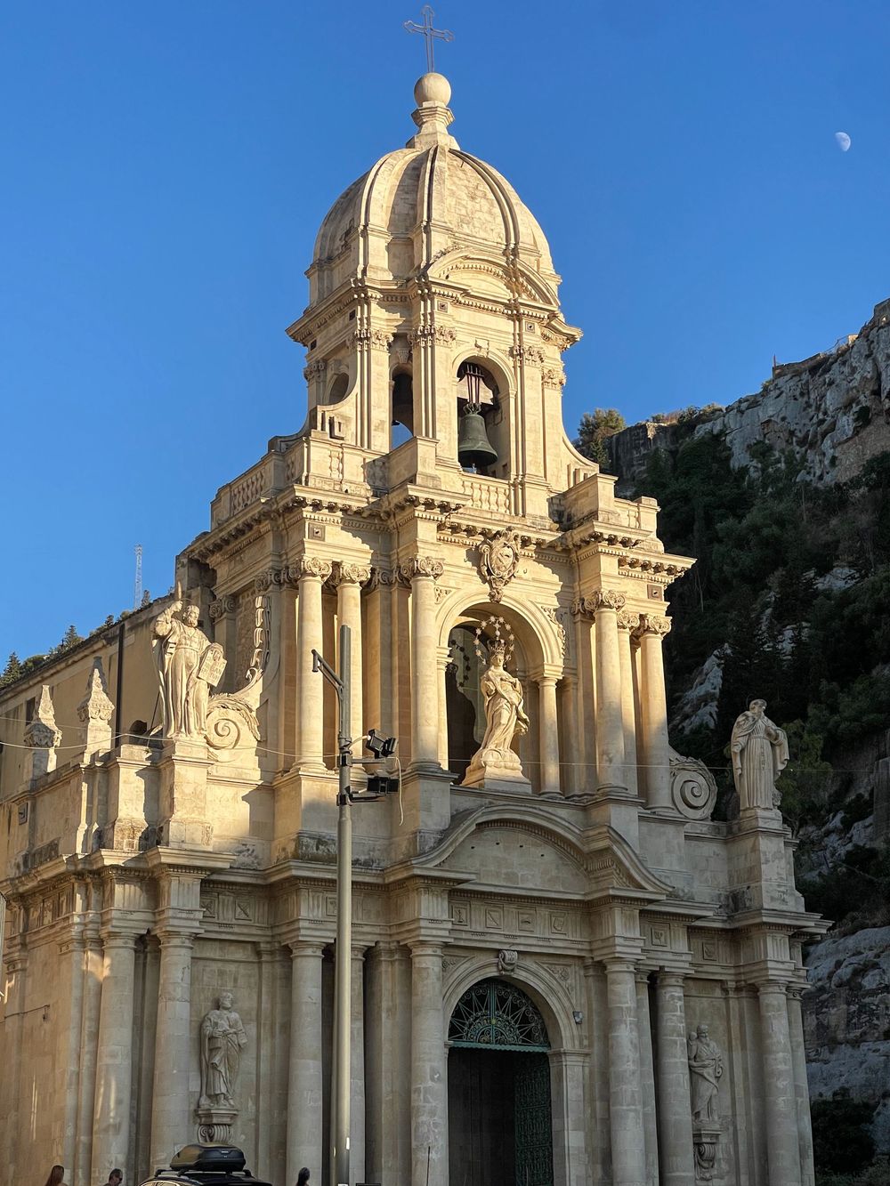 Four different views of a Baroque cathedral with golden stone façade and ornate domes against a bright blue sky in Sicily.