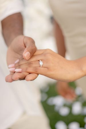Close-up of hands displaying an engagement ring with white floral petals in the background.