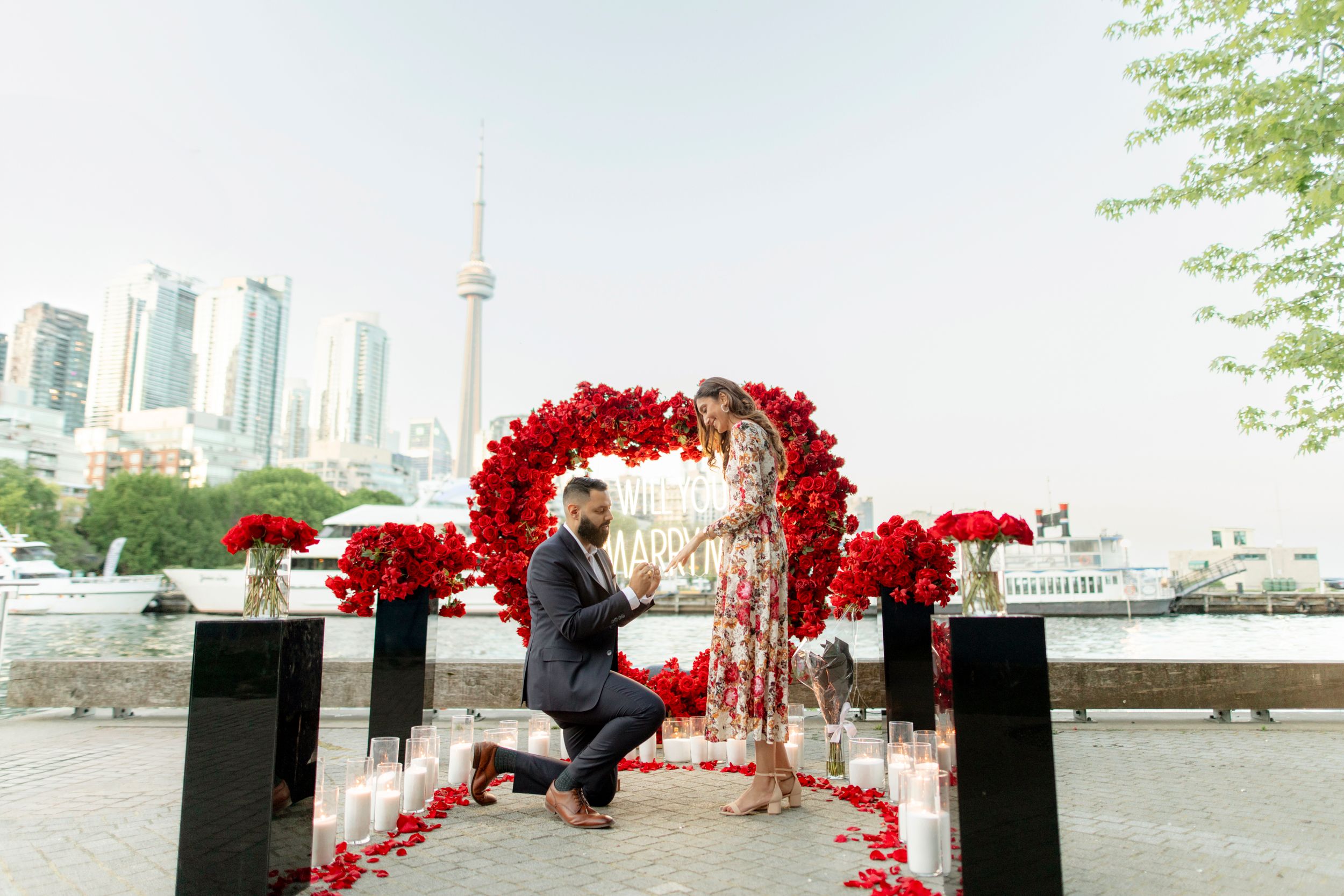 Marriage proposal setup with red floral arch and Toronto skyline in background.