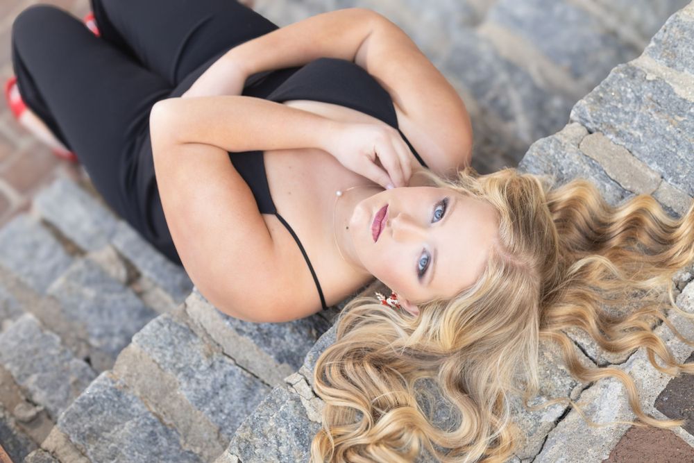 Senior with wavy blonde hair lies on stone steps while wearing a black top in an outdoor portrait. Kentucky senior photographer