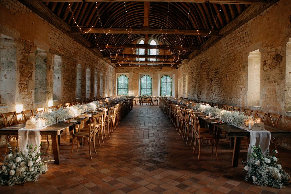 Elegant rustic wedding reception hall with long wooden tables, candles, and white floral centerpieces.