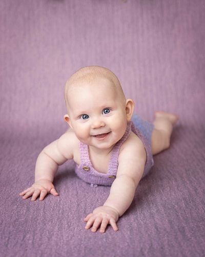 Smilende baby på 6 måneder med lilla body med lilla bakgrunn. Babytfotografering i studio på Fjerdingby på Romerike