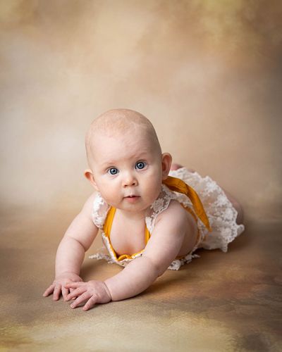 baby på 6 måneder med gul body med gul bakgrunn.Babyfotografering i studio på Fjerdingby på Romerike