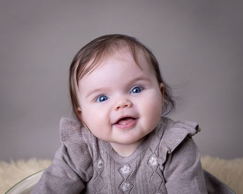Baby med brun kjole og grå bakgrunn. Babyfotografering i studio på Fjerdingby på Romerike