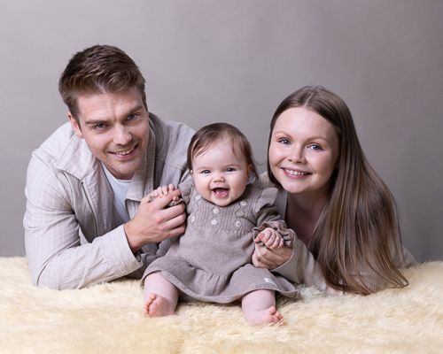 Familiebilde med brune klær på saueskinn med grå bakgrunn. Babyfotografering i studio på Fjerdingby på Romerike