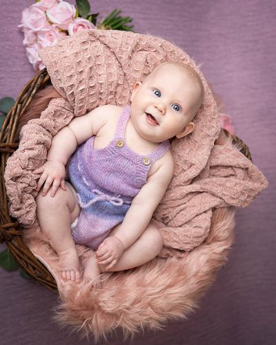 Smilende baby på 6 måneder med lilla body ligger på rosa teppe med lilla bakgrunn. Babyfotografering i studio på Fjerdingby på Romerike